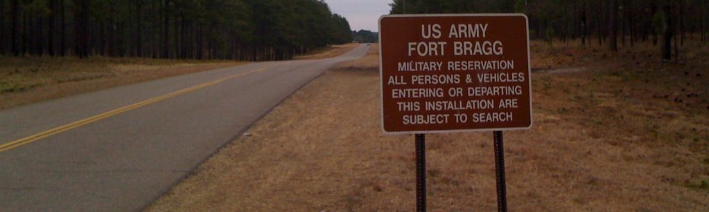 A road sign entering Fort Bragg going from Connecticut Avenue in Southern Pines, North Carolina, in March 2010. The sign reads, “US Army Fort Bragg Military Reservation – All persons and vehicles entering or departing this installation are subject to search.”