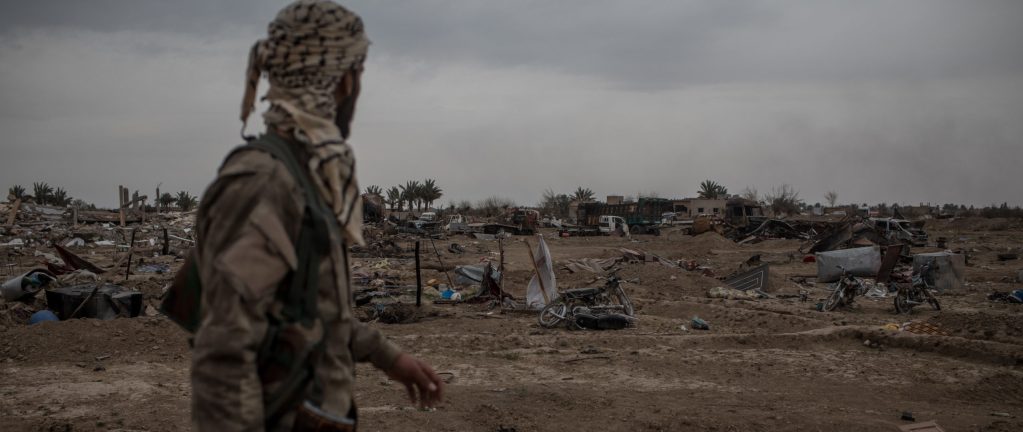 Image: BAGHOUZ, SYRIA - MARCH 24, 2019: A Syrian Democratic Forces (SDF) fighter walks past destroyed vehicles in the final ISIL encampment on March 24, 2019 in Baghouz, Syria. The Kurdish-led and American-backed Syrian Defense Forces (SDF) declared on March 23 the "100 percent territorial defeat" of the so-called Islamic State, also known as ISIS or ISIL. The group once controlled vast areas across Syria and Iraq, a population of up to 12 million, and a "caliphate" that drew tens of thousands of foreign nationals to join its ranks. (Photo by Chris McGrath/Getty Images)