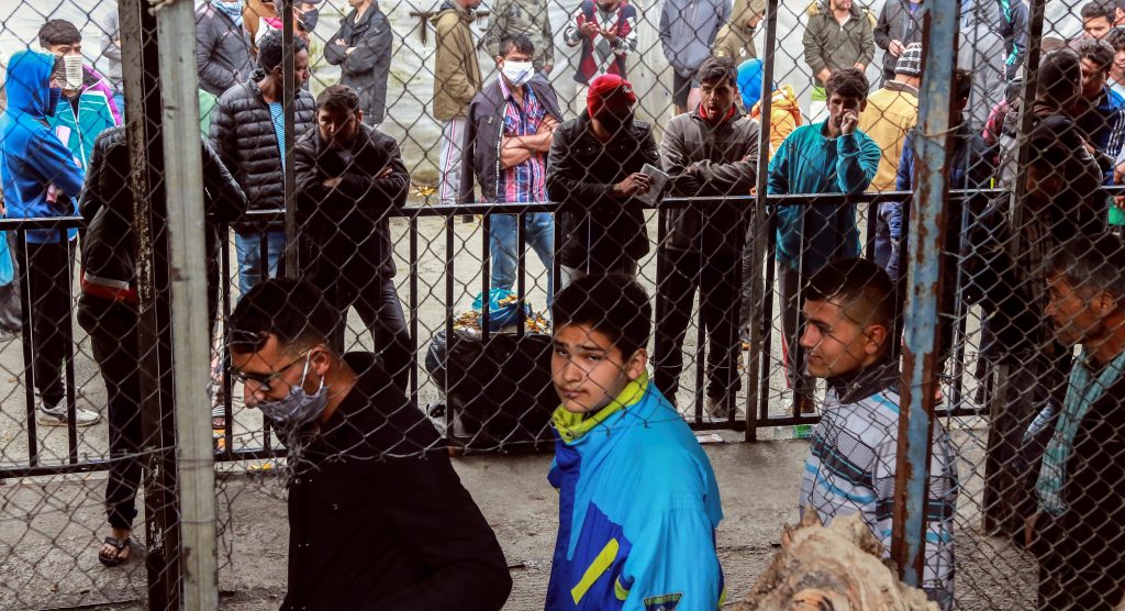 Migrants and refugees, some wearing facemasks for protective measures, queue in a makeshift camp next to the Moria camp on the Greek island of Lesbos.