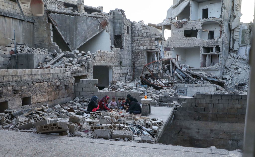 A displaced Syrian family breaks their fast together for the sunset "iftar" meal during Ramadan. They sit in the middle of the rubble of their destroyed home. May 4, 2020, Ariha, Idlib province