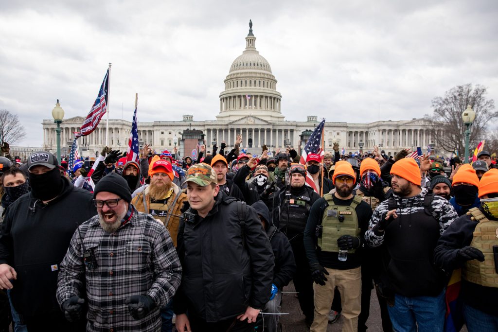 Members of the Proud Boys wearing orange hats stand in front of the U.S. capital.