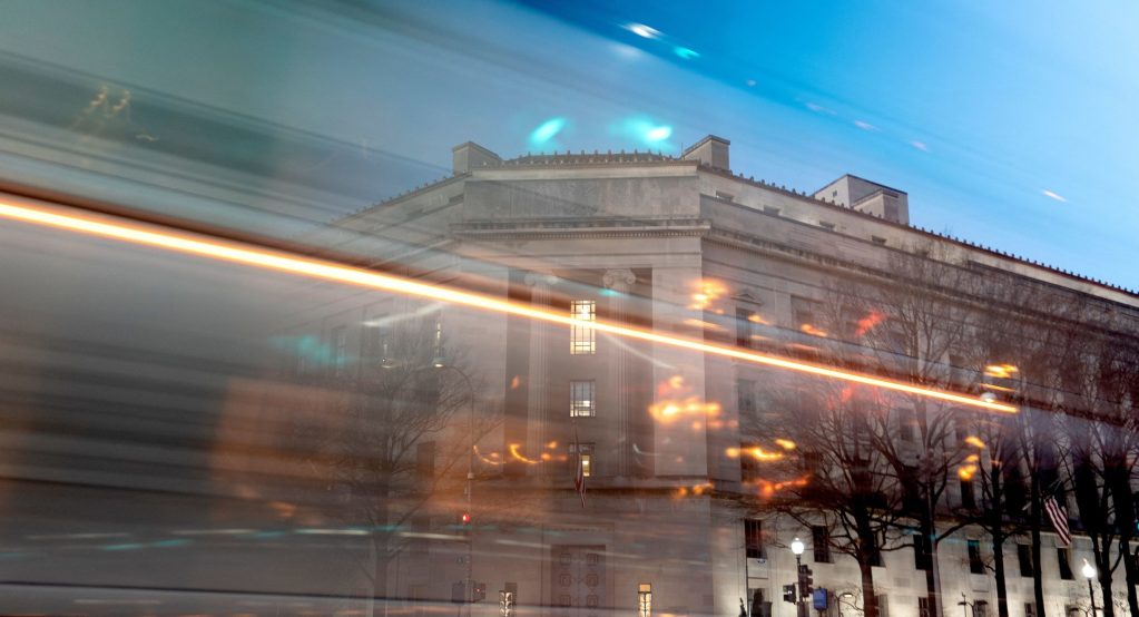 Department of Justice building in Washington, DC, with blurred lines of moving traffic in foreground