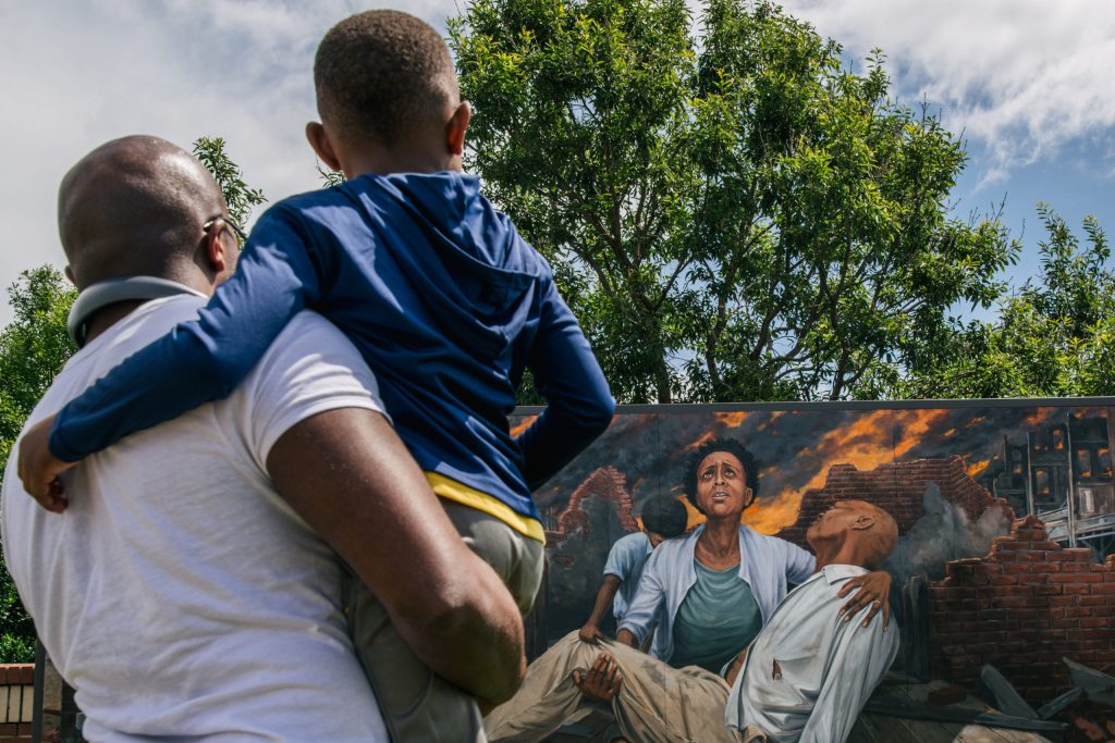 Nehemiah Frank holds his cousin David McIntye II as they stand in front of a mural depicting the violence of the Tulsa massacre and teaches him the history of the attack in the Greenwood district, on May 28, 2021 in Tulsa, Oklahoma.