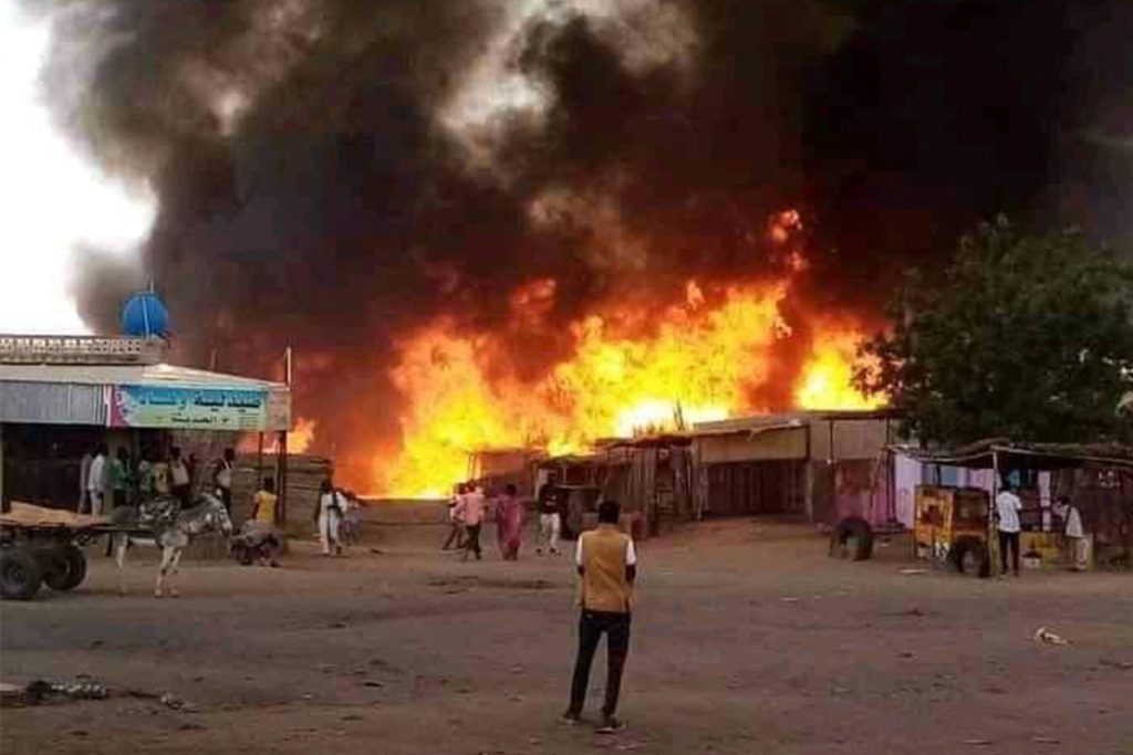 A fire blazes in a livestock market in the city of Al-Fashir in Sudan. There are yellow and orange flames rising into the sky.