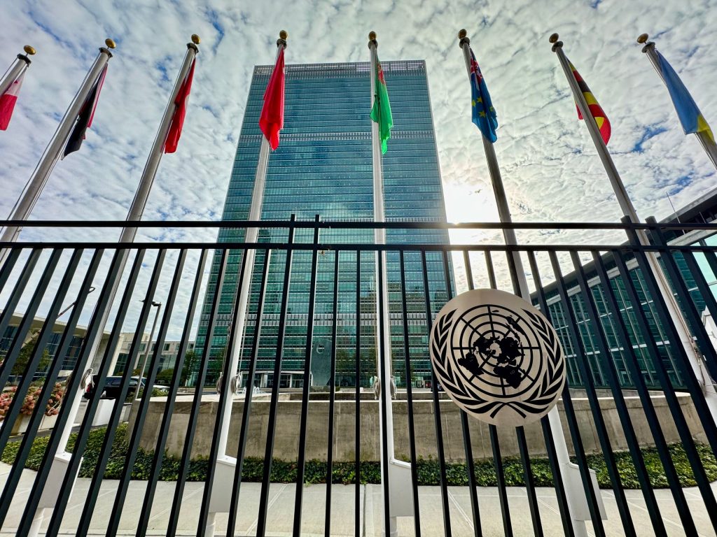 Various countries' flags in front of UN building and fence with UN symbol