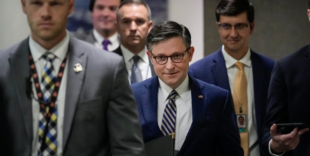 Men in suits walk down a hallway.