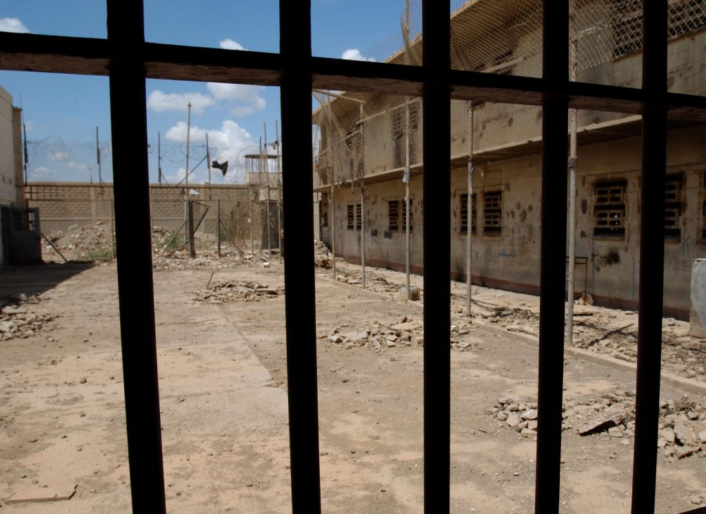 A courtyard in the Abu Ghrab is shown with prisoner cells on the sides. The photo is taken from behind a gate.