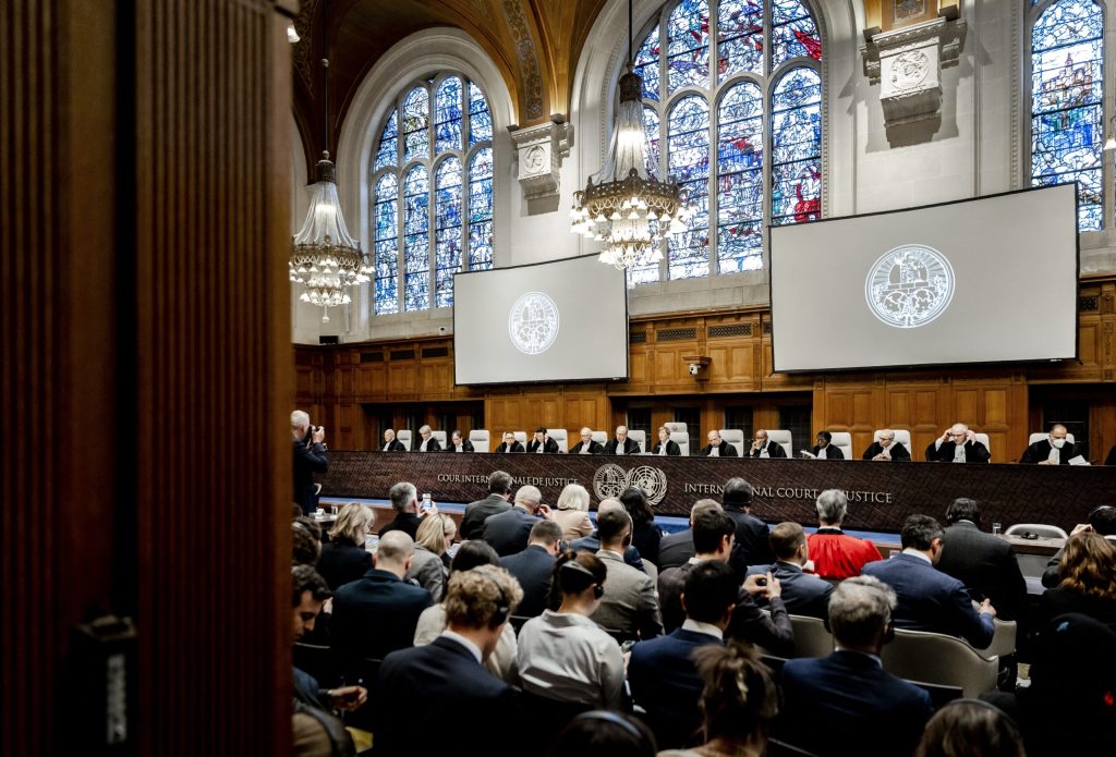 Wide-angle shot of long panel of judges in front of crowd, with two stained glass windows in background.