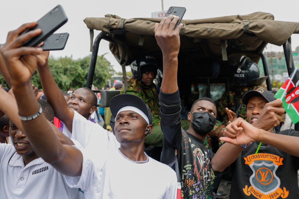Kenyan youths use mobile phone to record themselves next to a police van