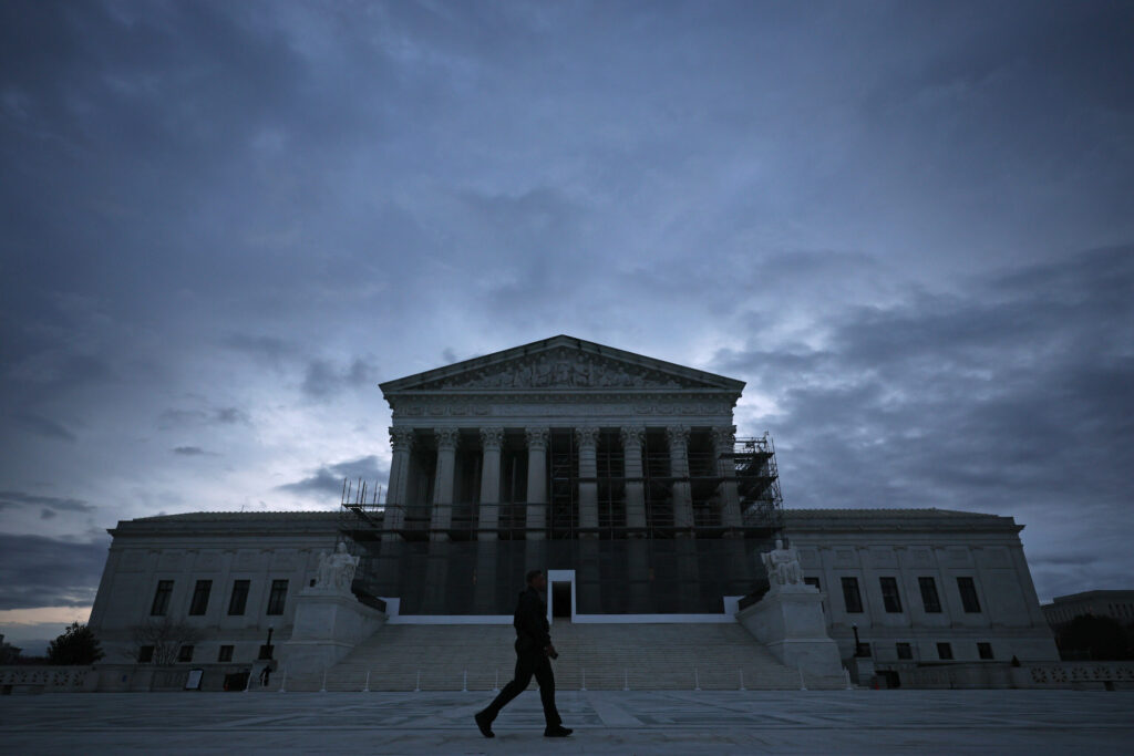 A man walks in front of the Supreme Court building at dusk.