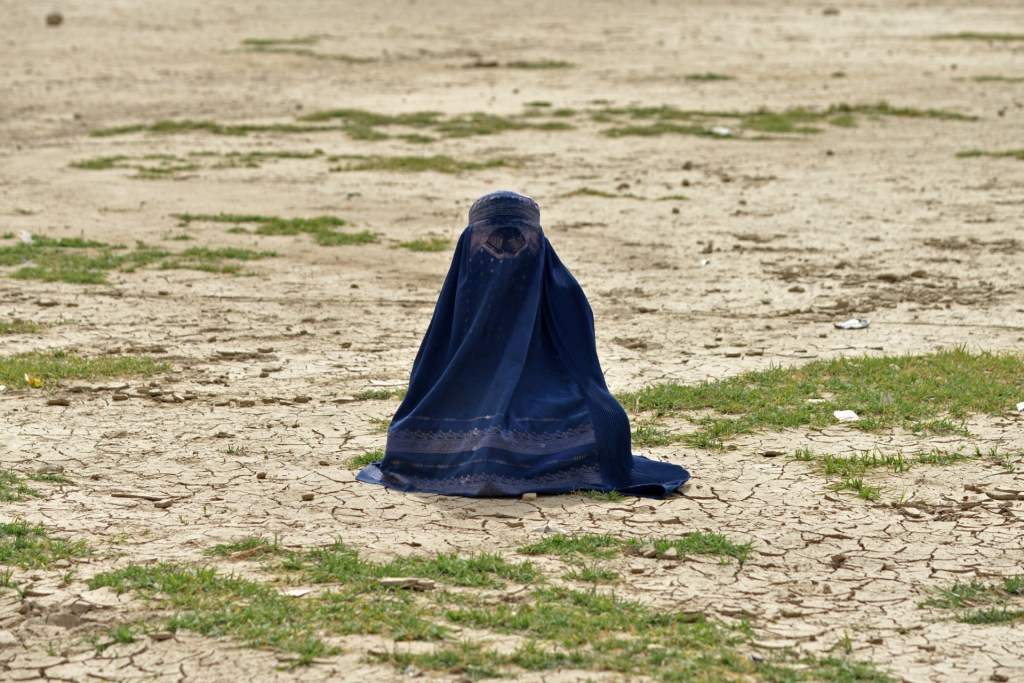 A burqa-clad woman sits in a field where a special prayer for rain is being performed by Afghan Muslims, in Fayzabad district of Badakhshan Province on May 19, 2025.
