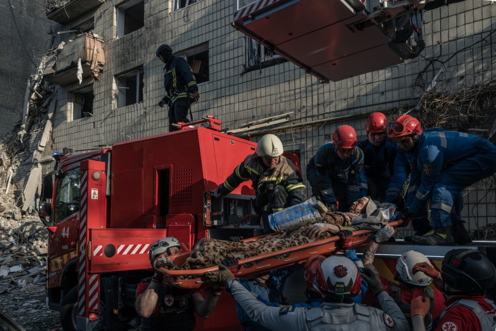 A wounded resident of a damaged apartment building is treated by medics