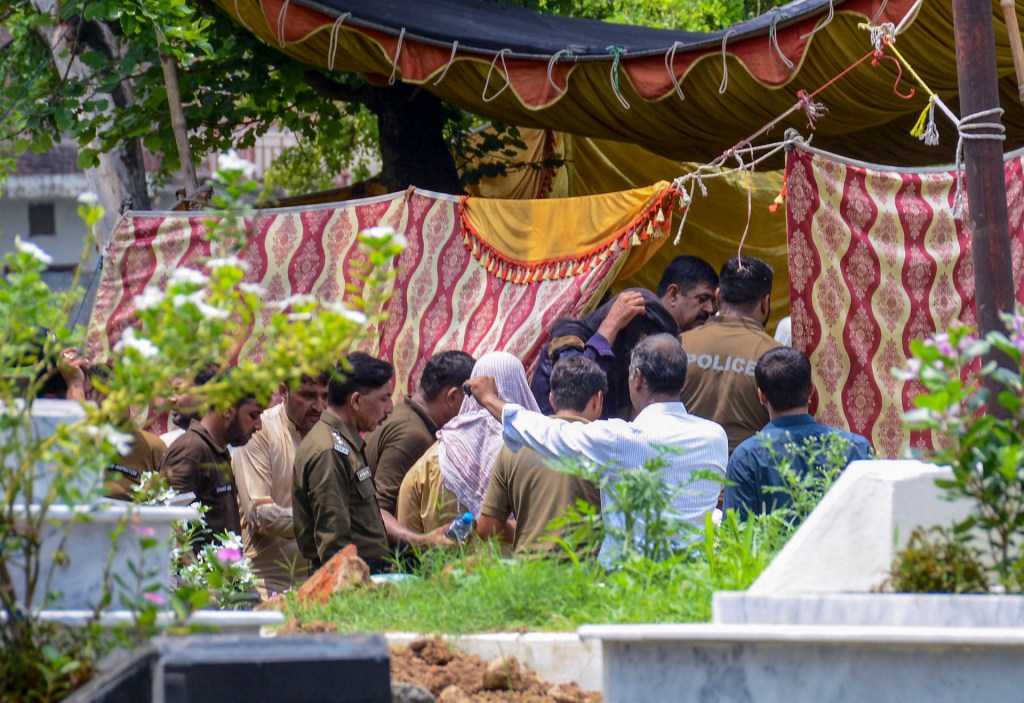 Police officers and medical team members gather at a cemetery in Rawalpindi, Pakistan, on July 28, 2025, as they begin the exhumation of a girl's grave. Authorities order the exhumation to conduct a post-mortem examination and establish the cause of death following allegations that the girl was killed under orders from a jirga, an informal tribal court. Suspects are brought to the site for identification as part of the investigation. The incident has sparked public outcry and renewed scrutiny over the role of illegal jirgas, which continue to operate outside the formal legal system in parts of Pakistan. Human rights activists condemn the extrajudicial process and call for legal reforms and stronger protections for women. The case underscores the ongoing challenges of enforcing state law in rural and semi-urban areas where customary practices still hold sway. (Photo by RAJA IMRAN/Middle East Images/AFP via Getty Images)