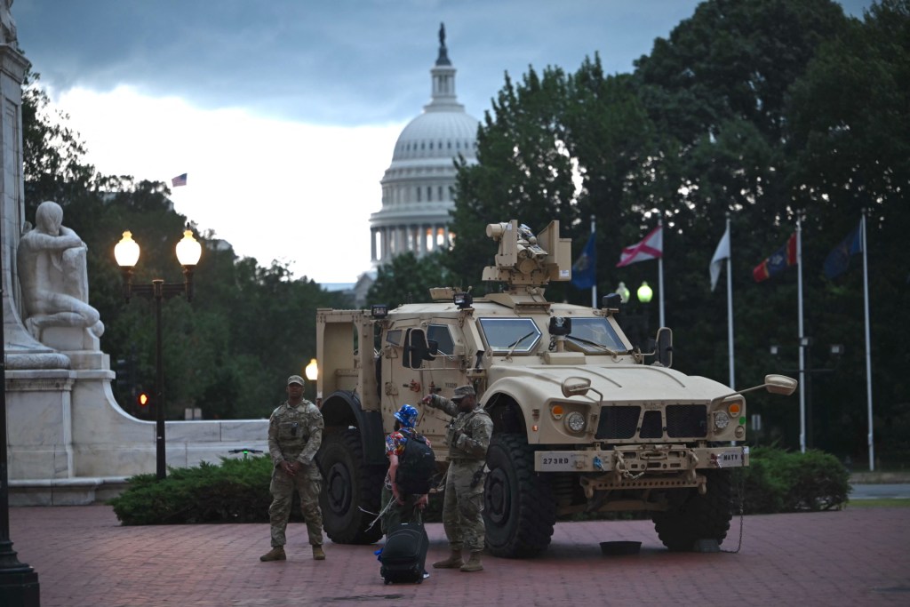 Members of the DC National Guard talk to a tourist outside Union Station as a storm approaches in Washington, DC, on August 17, 2025. US President Donald Trump on August 11 deployed military and federal law enforcement to curb violent crime in Washington, as he seeks to make good on his campaign pledge to be a "law and order" president. The Republican leader said he would place the city's Metropolitan Police under federal government control while also sending the National Guard onto the streets of the US capital. (Photo by Andrew Caballero-Reynolds / AFP) (Photo by ANDREW CABALLERO-REYNOLDS/AFP via Getty Images)