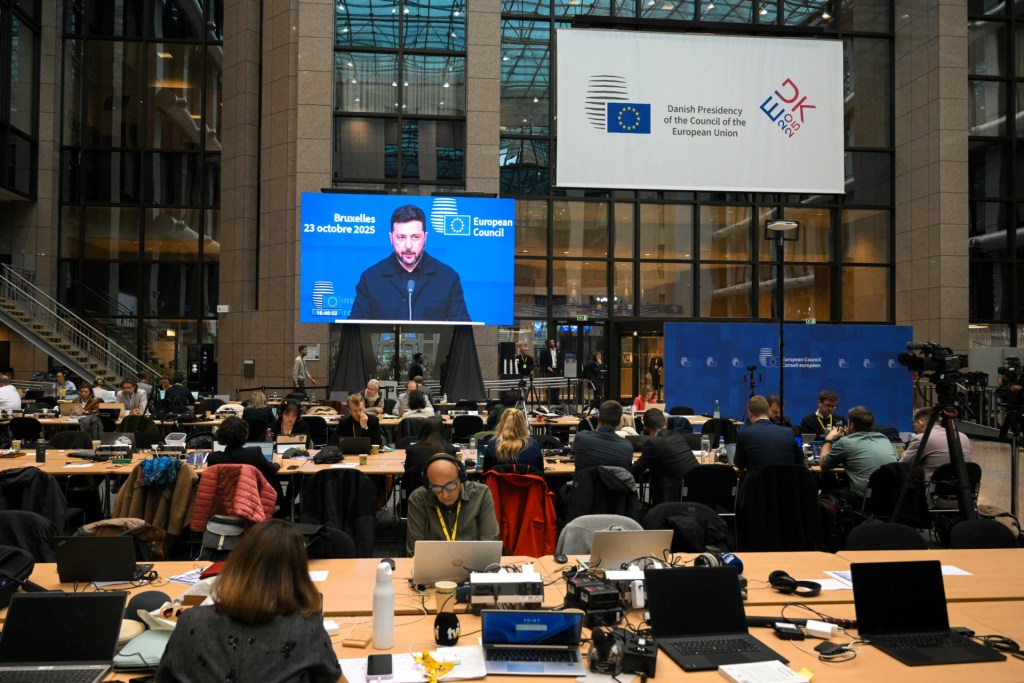 Journalists work as Ukraine's President Volodymyr Zelensky is seen on screen as he speaks to press during the European Council meeting gathering the 27 EU leaders to discuss Ukraine, European defence, and more, in Brussels, on October 23, 2025. (Photo by NICOLAS TUCAT / AFP) (Photo by NICOLAS TUCAT/AFP via Getty Images)