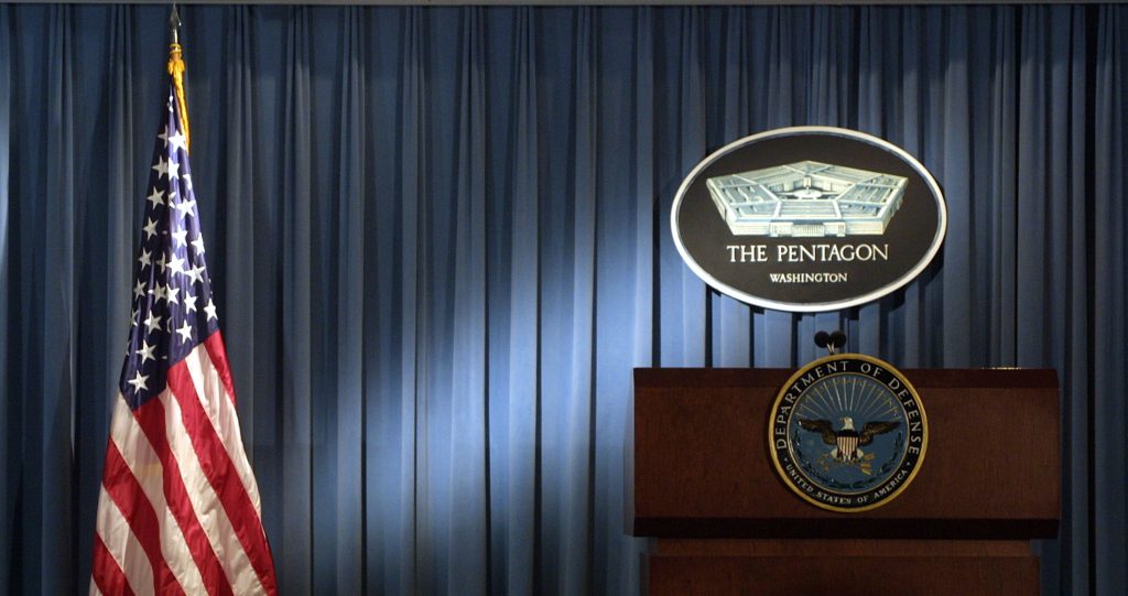 The Pentagon logo and an American flag are lit up in the briefing room of Pentagon in Arlington, VA.