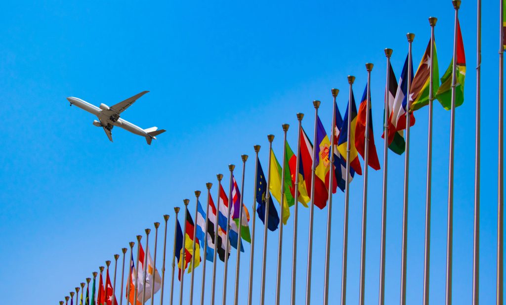 An airplane flies over a line of national flags.