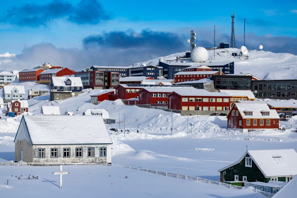The image shows multiple buildings, most of them non-residential, in white and red around a snowy hillside, with what appear to be cell phone and perhaps other types of steel towers and a radar atop the hill in the background.